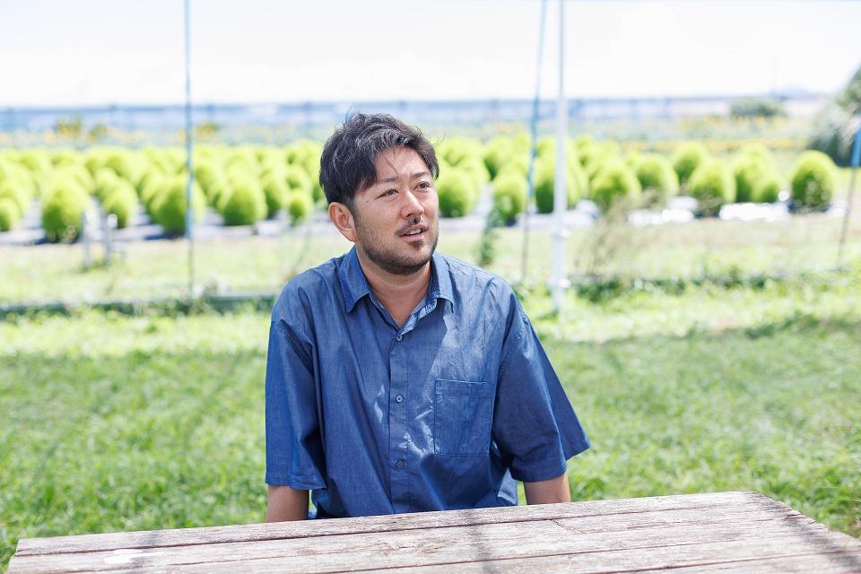 写真：緑の自然を背景に、青い半袖シャツを着た男性がインタビューを受けている様子